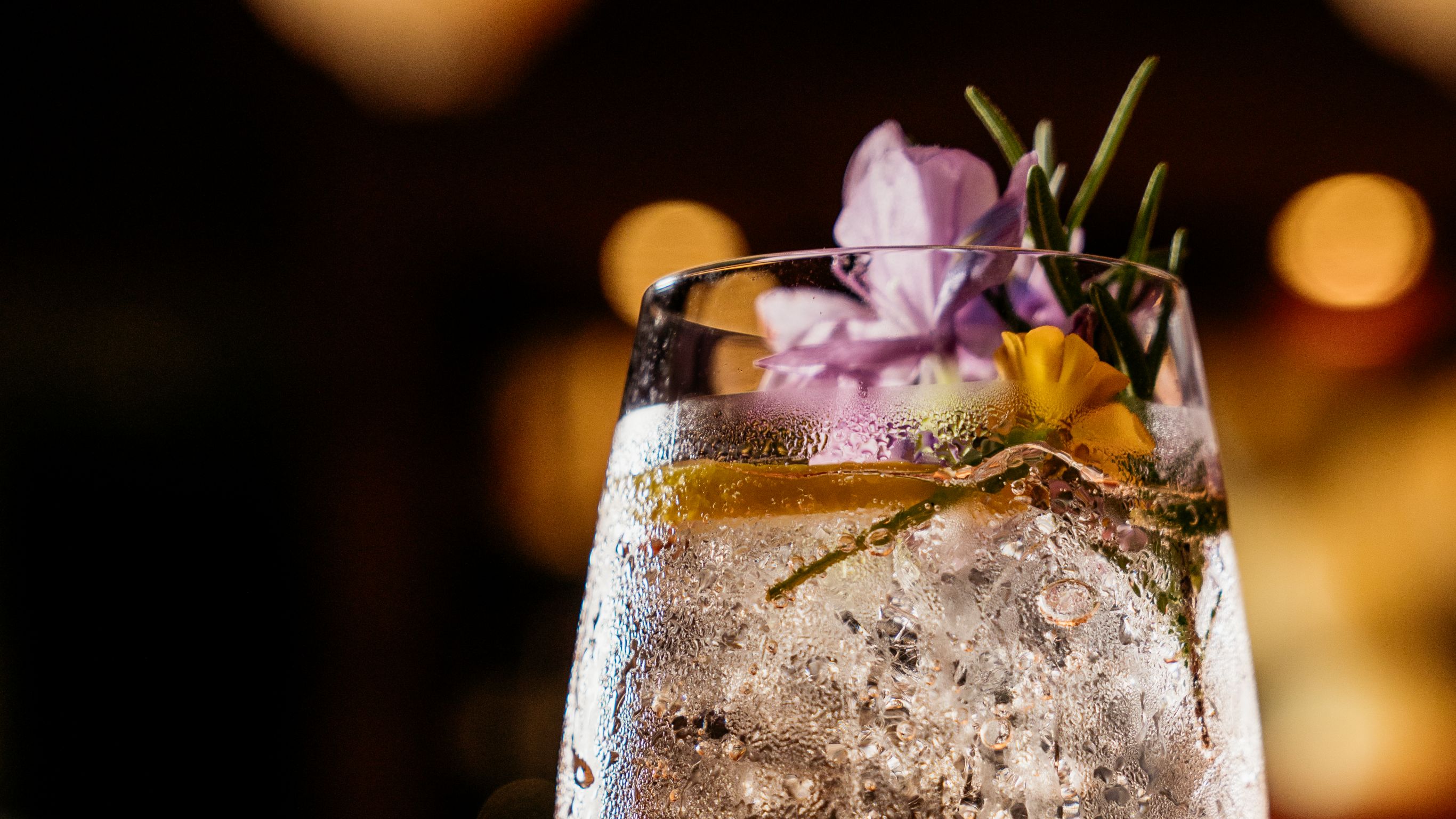 Zapote cocktail served in a tall Stem wine glass with purple flower garnish